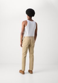 Tan chino's met een slim fit, witte tanktop en bruine schoenen. De chino's hebben riemlussen en achterzakken, met een fijne katoentextuur.