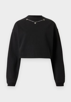 Črn skrajšan pulover z dolgimi rokavi in majhno srebrno verižico v bližini ovratu na belem ozadju.