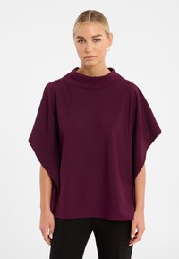 Lila poncho-artiger Oberteil mit hohem Kragen, Fledermausärmeln und weichem Stoff. Verfügt über einen geraden Saum und Seitenschlitze für Bewegungsfreiheit.