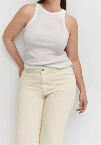 Top bianco senza maniche con scollatura rotonda, abbinato a jeans beige chiaro aderenti con tasche frontali e chiusura con bottone.