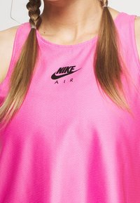 Femme portant un débardeur de sport Nike Air rose avec des cheveux tressés.