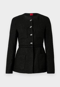 Zwarte tweedjas met een ronde halslijn, lange mouwen en zilveren knoopsluitingen. Heeft twee voorzakken en een gevlochten taille detail.