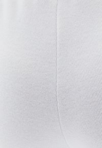Wit geribbeld stof met een fijne textuur, voorzien van verticale lijnen. Het materiaal is zacht en rekbaar, geschikt voor aangesloten kleding.