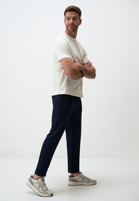 Chemise crème à manches courtes, pantalon azul cintré et baskets grises. Design simple, texture lisse et lignes épurées.