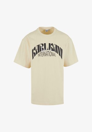 Camiseta de manga corta color crema con un cuello redondo que presenta el texto negro "KARL KANI INTERNATIONAL" en un diseño curvado y en negrita.