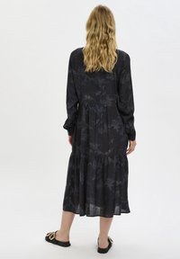 Długo-sleeve, ciemna sukienka w kwiatowy wzór z warstwowym dołem, posiadająca dopasowaną talię i miękką, zwiewną tkaninę. Połączona z czarnymi płaskimi sandałami.