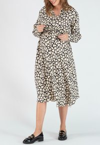 Langarmhemdkleid in Creme mit unregelmäßigem Schwarzmuster, tailliert. Kombiniert mit schwarzen Slippern, die einen entspannten Sitz zeigen.