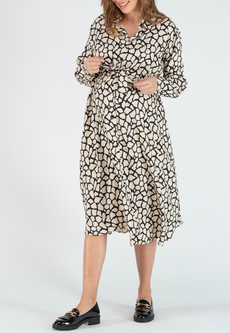 Langarmhemdkleid in Creme mit unregelmäßigem Schwarzmuster, tailliert. Kombiniert mit schwarzen Slippern, die einen entspannten Sitz zeigen.