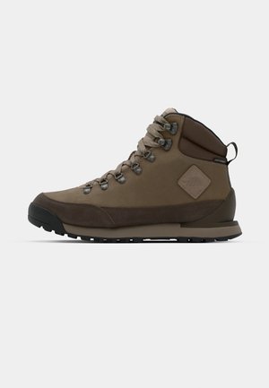 Brązowy, średniej wysokości but trekkingowy wykonany z skóry i materiału tekstylnego, z metalowymi oczkami, sznurówkami, wyściółką wokół kostki oraz wytrzymałą czarną gumową podeszwą.