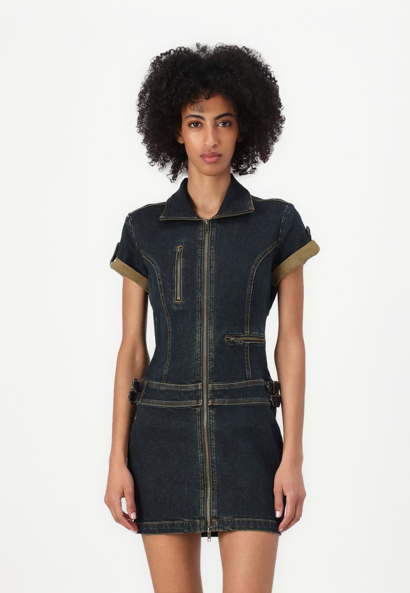 Denimdress med kortermede ermer, en frontglidelås og to lommer. Har et mørkeblått stoff med kontrasterende gule sømmer og mansjettdetaljer.