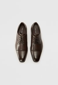 Scarpe eleganti in pelle marrone con punta affusolata, superficie liscia e più fori per i lacci, caratterizzate da un delicato dettaglio di cucitura sul davanti.