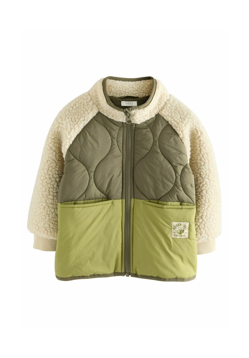 Veste matelassée verte avec manches en polaire crème, deux poches avant et fermeture éclair. Elle présente un patch logo sur le bas à gauche.