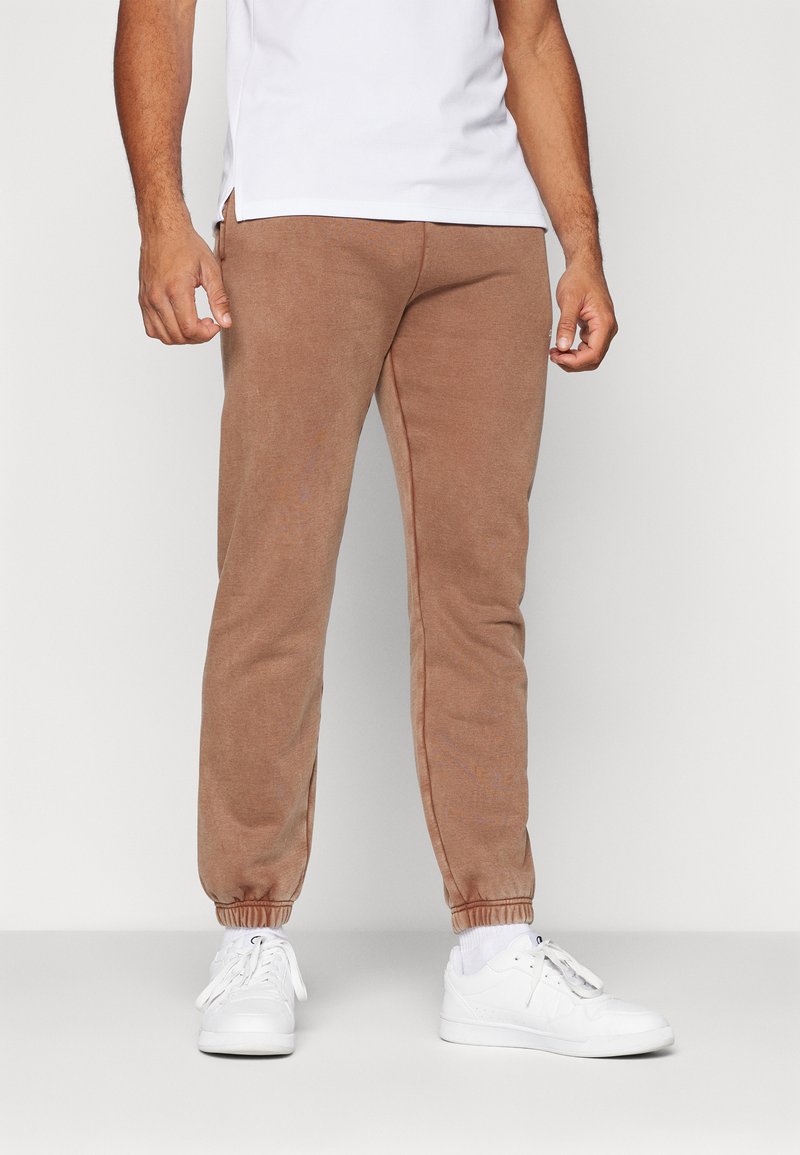 Brune jersey sweatpants har en tætsiddende pasform, elastiske manchetter og en glat tekstur. Bæres med hvide sneakers for kontrast.