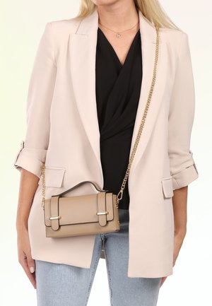 Woman wearing a light beige blazer over a black top and light blue jeans, carrying a beige crossbody bag with a gold chain strap.