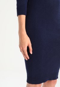 Abito in maglia a coste navy con maniche a tre quarti, caratterizzato da una silhouette aderente e una finitura testurizzata. L'orlo presenta un delicato dettaglio a coste.