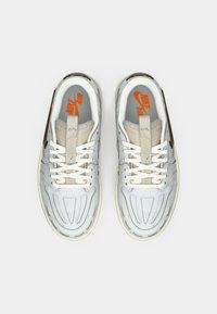 Sneakers Nike Air con tomaia in pelle azzurro chiaro, con lacci bianchi e dettagli beige. Linee di ventilazione laterali e logo ben visibili.