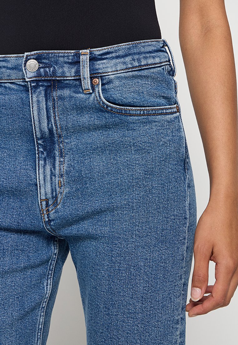 Hochtaillierte blaue Jeans aus Denim mit glatter Textur, Fünf-Taschen-Design sowie kontrastierenden kupferfarbenen Nähten und Hardware-Details.