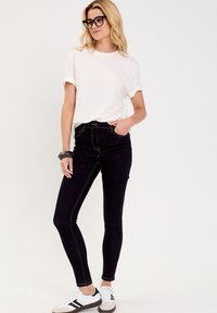 Jeans noirs taille haute avec des coutures contrastées, associés à un t-shirt blanc ample et des baskets blanches avec des accents noirs.