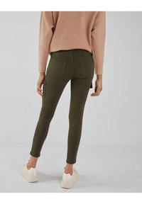 Olivgröna stretchnylonjeans med en kroppsnära design, som har två bakfickor och en sidofickor. Kombineras med en ljusrosa tröja.