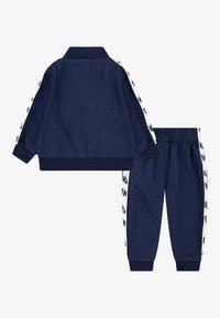 Σετ φόρμας σε ναυτικό μπλε χρώμα με ζακέτα που κλείνει με φερμουάρ, με ριμπ γιακά και μανσέτες, και παντελόνι με ελαστική μέση, και τα δύο διακοσμημένα με λευκές ρίγες στα πλάγια.