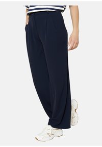 Navy wide-leg trousers made of lightweight fabric with pleats, featuring side pockets and a relaxed fit, paired with white sneakers.