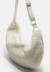 Crème-kleurige schoudertas van zacht, getextureerd materiaal. Gebogen vorm met een brede opening en een verstelbare strap in een contrasterende lichte kleur.