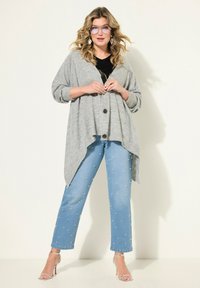 Cardigan grigio con vestibilità oversize, chiusura a bottoni, abbinato a jeans azzurri decorati con perline argento e sandali con tacco trasparente.