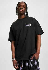 Tricou negru cu mânecă scurtă, având un logo "puma" brodat în violet pe pieptul stâng; material din bumbac cu croială lejeră.