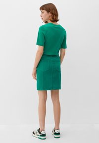 T-shirt en coton vert à manches courtes associé à une jupe en denim vert, dotée de deux poches arrière. Des baskets noir et blanc complètent le look.