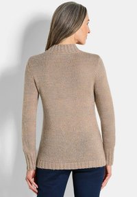 Pull en maille beige à manches longues, avec col et ourlet côtelés. Présente un motif texturé et une coupe décontractée, associé à un pantalon sombre.