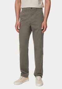Olivegrüne Baumwollhose mit geradem Schnitt, Knopfverschluss und G�ürtelschlaufen, kombiniert mit beigen Sneakers. Sanfte Textur, ohne Muster.