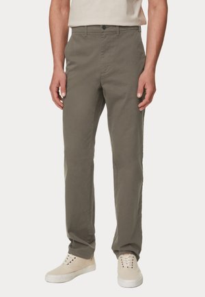 Pantaloni in cotone verde oliva a vestibilità dritta, con chiusura a bottoni e passanti per cintura, abbinati a sneakers beige. Tessuto liscio, senza fantasie.
