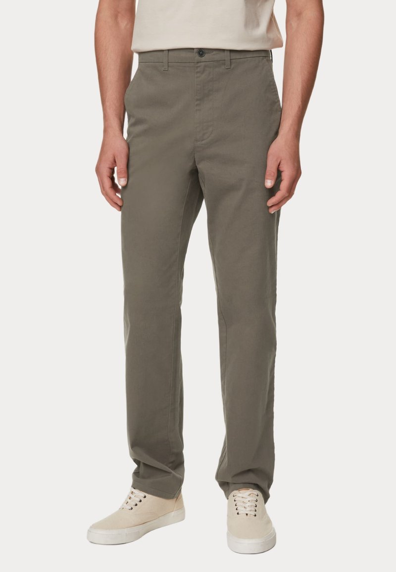 Olivegrüne Baumwollhose mit geradem Schnitt, Knopfverschluss und Gürtelschlaufen, kombiniert mit beigen Sneakers. Sanfte Textur, ohne Muster.