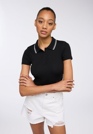 Polo shirt nero a coste con colletto, caratterizzato da righe bianche e chiusura a bottoni, abbinato a pantaloni corti in denim bianco rovinati.