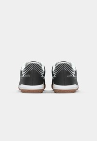 Black athletic shoes with white accents, featuring a textured upper, a gum rubber sole, and a geometric pattern on the back.