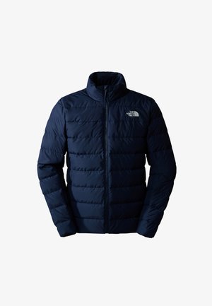 Navy blue puffer jacket with a high collar, zip closure, and horizontal quilting. Features a small, white logo on the upper left chest.