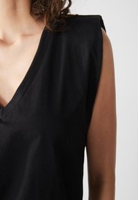 Schwarzes V-Ausschnitt-Oberteil mit kurzen, strukturierten Ärmeln, aus weichem Stoff. Glatte Textur mit minimalistischen Design, ohne sichtbare Muster oder Akzente.