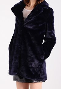 Abrigo de piel sintética color navy con un amplio cuello, mangas largas y dos bolsillos frontales. Textura suave y diseño elegante, adecuado para un look casual.