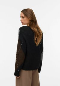 Prevelik črn pleten pulover s sivimi in rjavimi diamantnimi vzorci. Ima okrogli izrez in kontrastne šive na rokavih.