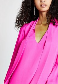 Blusa leggera rosa con scollatura a V e maniche fluttuanti. Tessuto morbido e vestibilità ampia, che si adagia elegantemente sulle spalle.