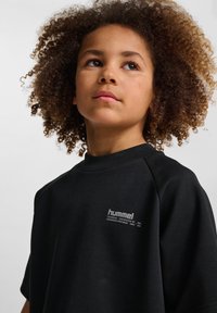Sort kortærmet sweatshirt lavet af blødt stof med rund halsudskæring. Udstyret med et hvidt logo foran. Simpelt design, ingen mønstre.