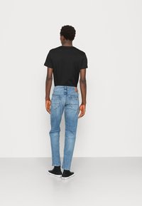 Heren blauwe denim jeans met een rechte snit, voorzien van een lichte wassing, vijf zakken en een leren logo patch op de achterkant. Gepaarde met een zwart t-shirt.