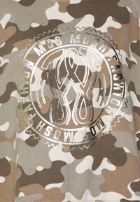 Sweatshirt med camouflage-mönster i jordtoner med en metallisk grafisk design som har cirkulär text och flytande former i mitten.