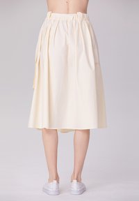 Jupe jaune pâle longueur genou avec une taille froncée, des poches latérales et une texture lisse, associée à des baskets blanches.