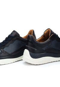 Baskets noires en cuir et maille avec des accents navy, des panneaux texturés et une semelle blanche ornée d'un motif sur le bord.