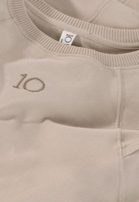 Felpa beige con scollatura rotonda, tessuto testurizzato e un dettaglio ricamato "10" in una tonalità più scura sul davanti.
