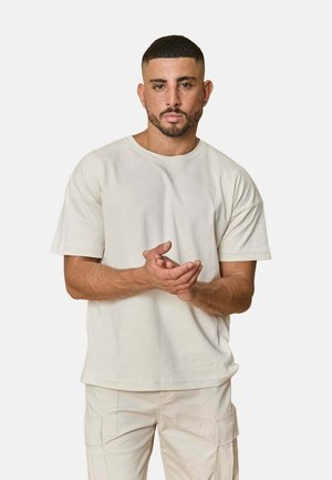 T-shirt beige clair à manches courtes avec un col rond, fabriqué en tissu doux, présentant une coupe décontractée et un ourlet droit. Aucune motif visible.