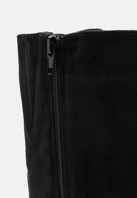 Bottine en daim noir à texture lisse, dotée d'une fermeture éclair latérale et d'un design élégant et effilé.