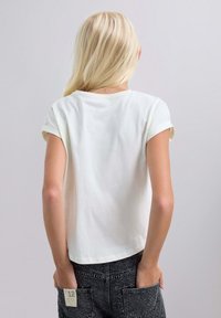 Tricou alb din bumbac cu mâneci scurte răsucite, guler rotund și o croială relaxată, asortat cu blugi negri uzați cu buzunare pe spate.