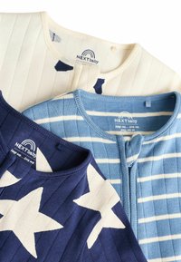 Trois bodies pour bébés : crème avec des étoiles navy, bleu clair avec des rayures et bleu foncé avec un côtelé ; tous présentent des encolures arrondies et des étiquettes en tissu.